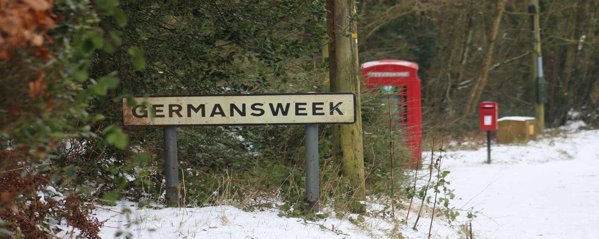 The phone box and post box in the snow behind the Germansweek village sign. 